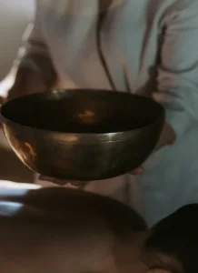 Person holding a large metal bowl over someone lying down.